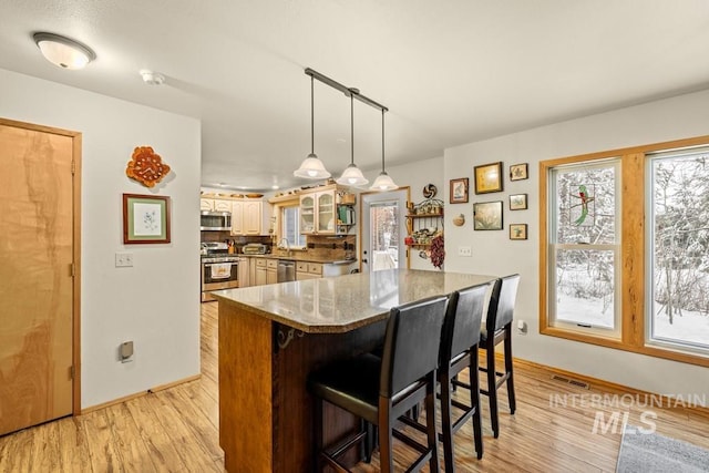 kitchen with appliances with stainless steel finishes, stone countertops, light hardwood / wood-style flooring, a breakfast bar, and a center island