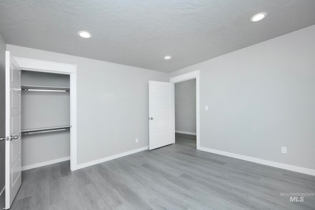 unfurnished bedroom with recessed lighting, a closet, a textured ceiling, wood finished floors, and baseboards