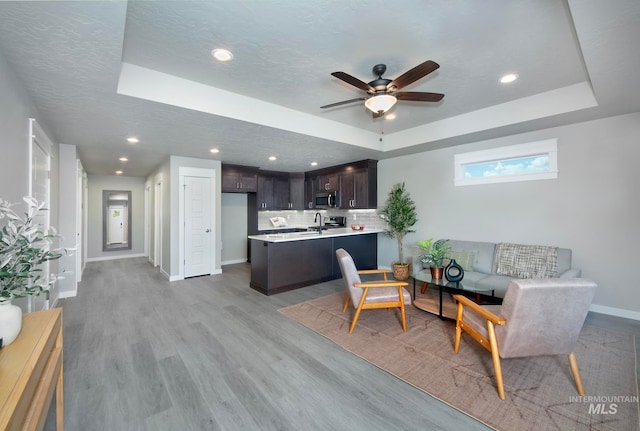 living area featuring baseboards, a tray ceiling, and light wood-style floors