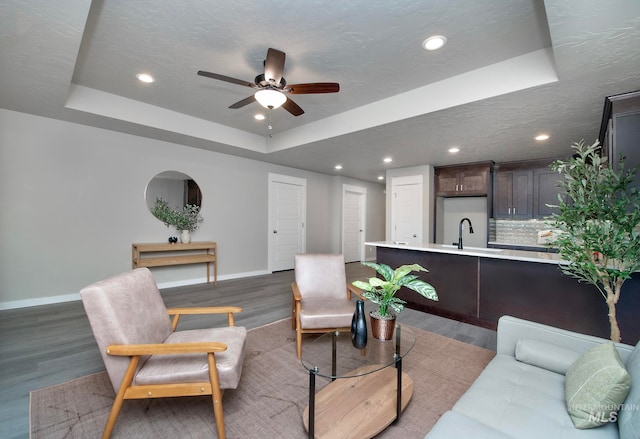 living area featuring dark wood-style floors, baseboards, a raised ceiling, and a textured ceiling