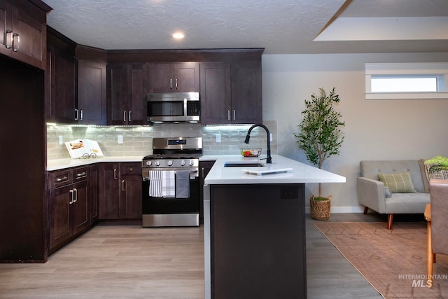 kitchen with decorative backsplash, appliances with stainless steel finishes, light countertops, light wood-type flooring, and a sink