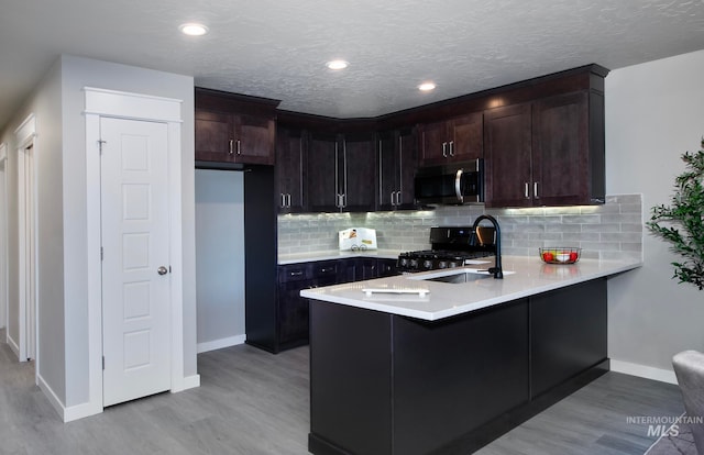 kitchen with a peninsula, a sink, light countertops, range, and stainless steel microwave