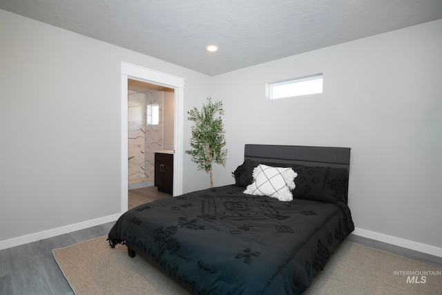 bedroom featuring connected bathroom, multiple windows, baseboards, and wood finished floors