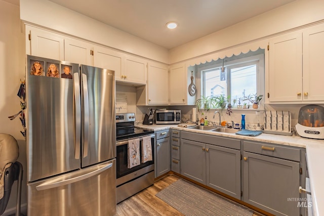 kitchen featuring sink, stainless steel appliances, gray cabinets, white cabinets, and light wood-type flooring