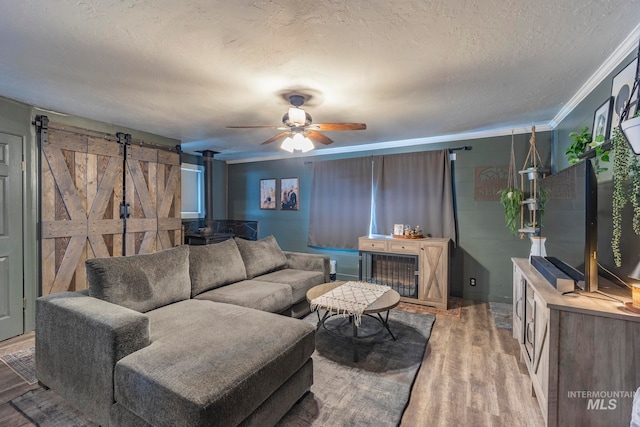 living room featuring hardwood / wood-style flooring, ceiling fan, a barn door, ornamental molding, and a textured ceiling