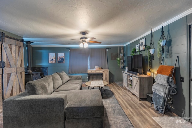 living room with ceiling fan, a barn door, crown molding, a textured ceiling, and hardwood / wood-style flooring