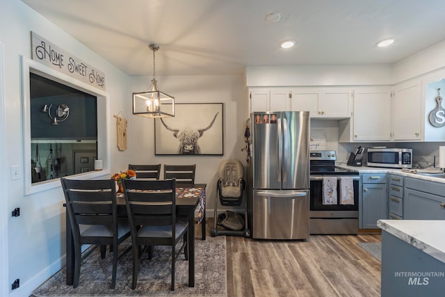 kitchen with appliances with stainless steel finishes, a chandelier, pendant lighting, white cabinets, and hardwood / wood-style flooring