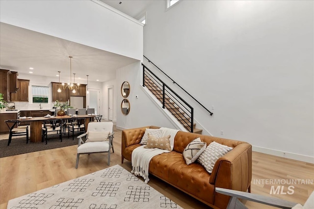 living room featuring light wood finished floors, baseboards, stairway, and a notable chandelier