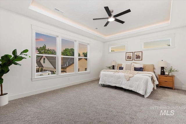 carpeted bedroom with a tray ceiling, visible vents, ceiling fan, and baseboards