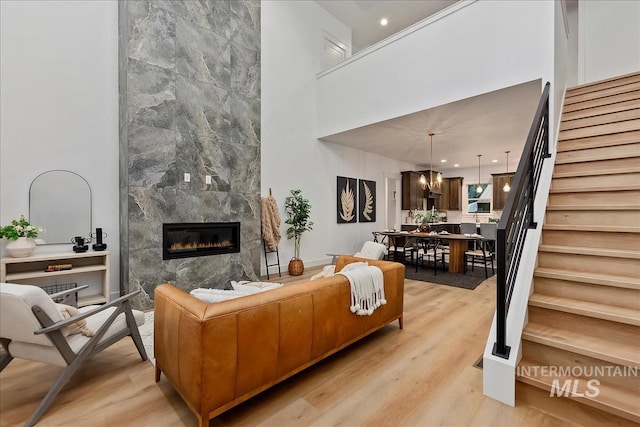 living room with a towering ceiling, light wood-style floors, stairs, and a premium fireplace