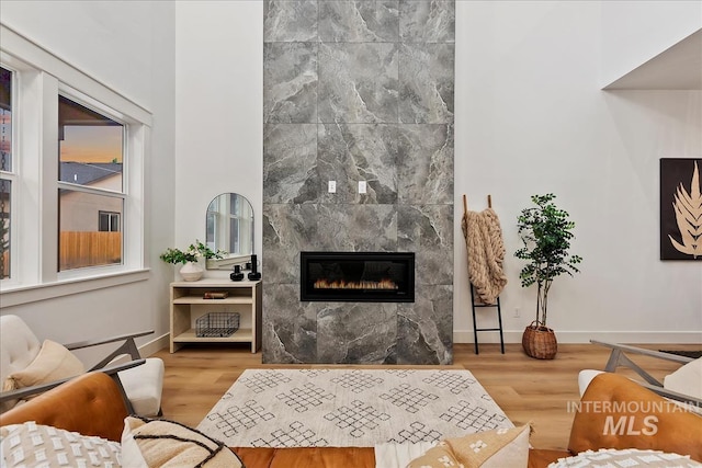 living area with a tile fireplace, baseboards, and wood finished floors