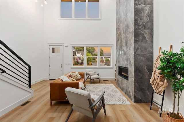 living room featuring wood finished floors, a towering ceiling, visible vents, stairway, and a tiled fireplace