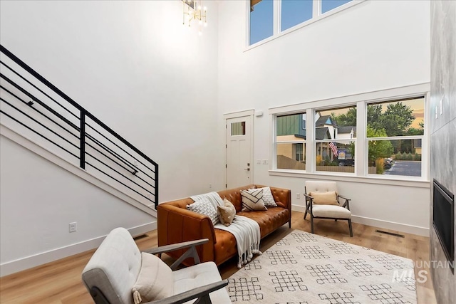 living area with baseboards, a towering ceiling, light wood finished floors, and stairs