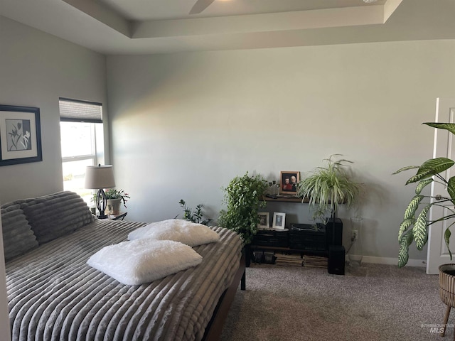 carpeted bedroom with a tray ceiling and baseboards