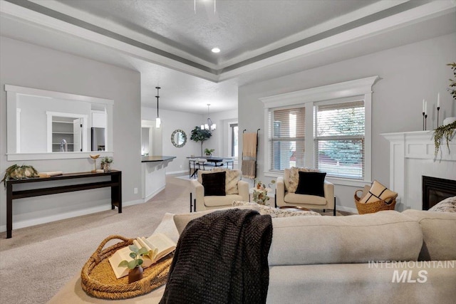 living area featuring a chandelier, a raised ceiling, a glass covered fireplace, carpet, and baseboards