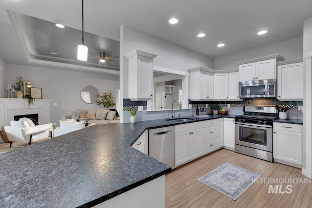 kitchen with white cabinets, a sink, dark countertops, stainless steel appliances, and a fireplace
