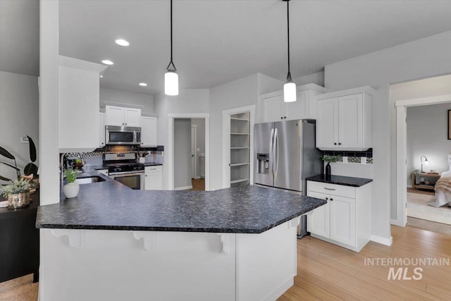 kitchen with stainless steel appliances, dark countertops, backsplash, a sink, and white cabinetry
