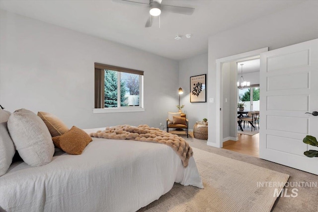 bedroom featuring light colored carpet, baseboards, and ceiling fan with notable chandelier