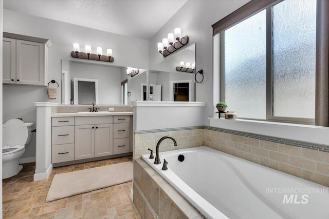 bathroom with vanity, toilet, stone finish floor, baseboards, and a garden tub