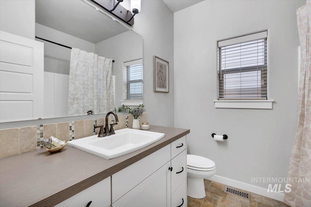 full bathroom with stone finish floor, visible vents, baseboards, toilet, and vanity