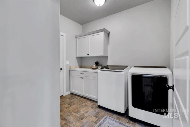 washroom featuring baseboards, cabinet space, washing machine and clothes dryer, and stone finish flooring