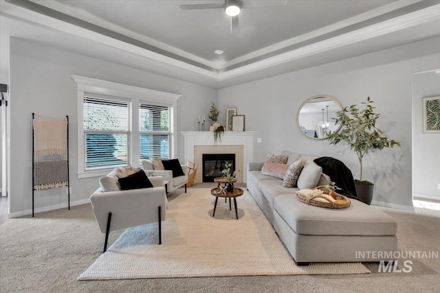 carpeted living area with baseboards, ceiling fan, a tray ceiling, and a glass covered fireplace