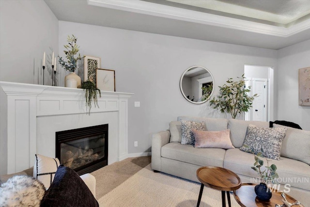 carpeted living room featuring a glass covered fireplace and a raised ceiling