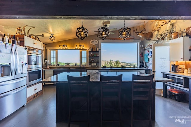 kitchen with vaulted ceiling, pendant lighting, stainless steel appliances, and white cabinets