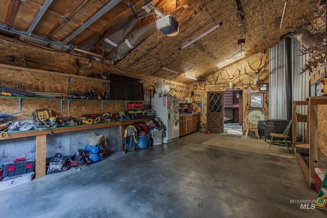 garage featuring a garage door opener, a workshop area, and white refrigerator with ice dispenser