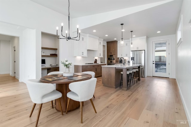 dining space with sink, vaulted ceiling, a chandelier, and light wood-type flooring