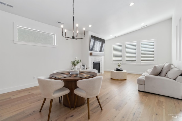 dining room with a notable chandelier, a fireplace, vaulted ceiling, and light wood-type flooring