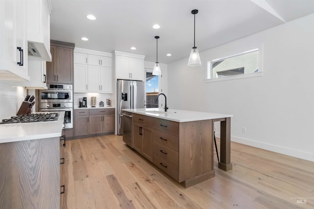 kitchen with sink, appliances with stainless steel finishes, an island with sink, pendant lighting, and white cabinets