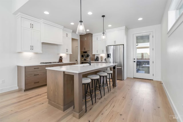 kitchen featuring appliances with stainless steel finishes, pendant lighting, white cabinetry, an island with sink, and backsplash