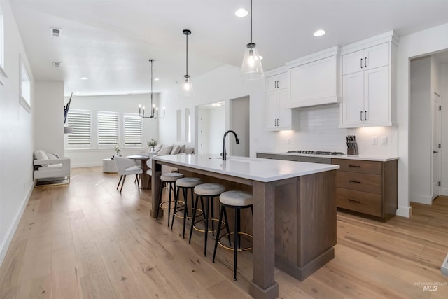 kitchen featuring a large island, sink, hanging light fixtures, white cabinets, and decorative backsplash