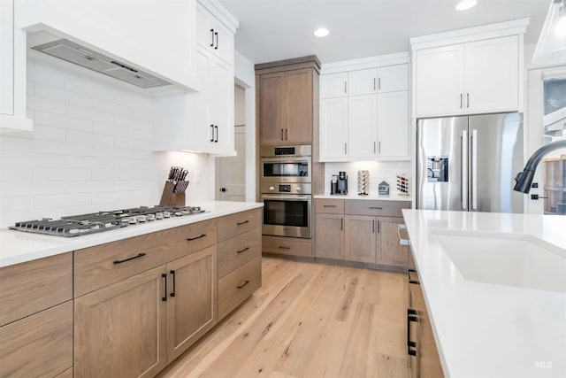 kitchen with appliances with stainless steel finishes, sink, white cabinets, light hardwood / wood-style floors, and custom range hood