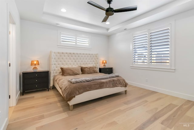 bedroom featuring a raised ceiling, ceiling fan, and light wood-type flooring