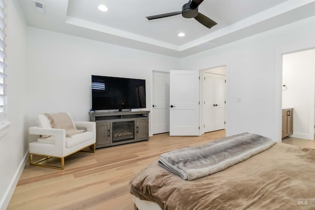 bedroom with a raised ceiling, ceiling fan, and light hardwood / wood-style flooring