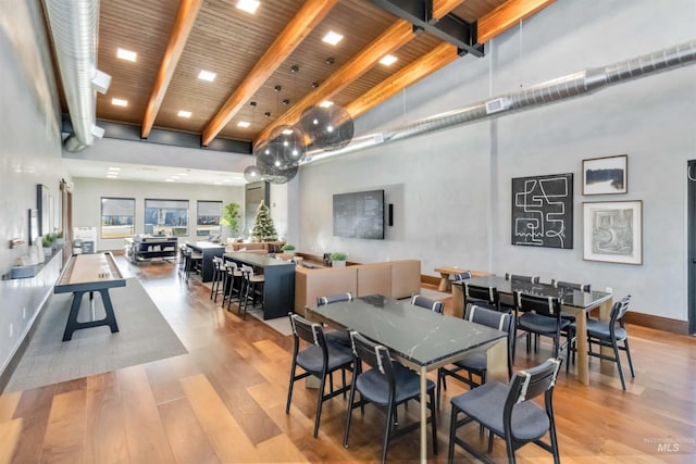 dining space with beamed ceiling, a towering ceiling, wood ceiling, and light hardwood / wood-style flooring