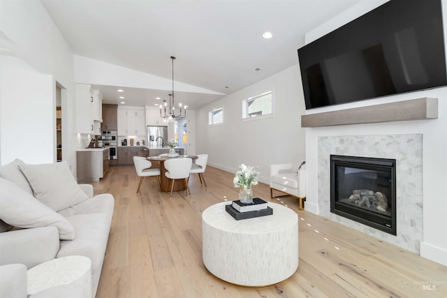 living room with a notable chandelier, vaulted ceiling, a premium fireplace, and light wood-type flooring