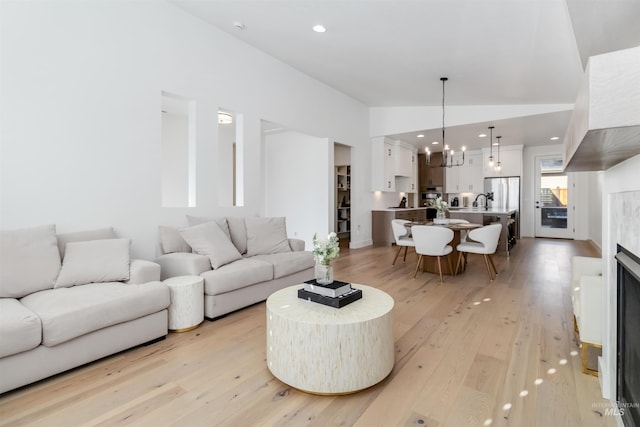 living room with lofted ceiling, a notable chandelier, and light hardwood / wood-style floors