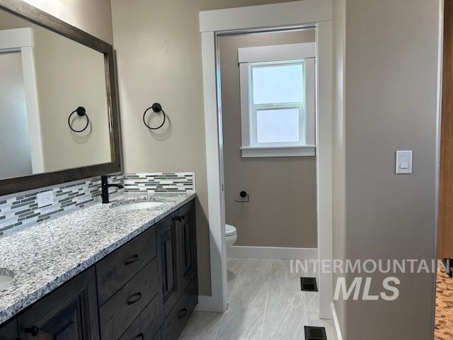 bathroom featuring toilet, vanity, and tasteful backsplash