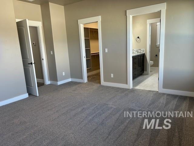 unfurnished bedroom featuring ensuite bath, light colored carpet, a closet, and a spacious closet