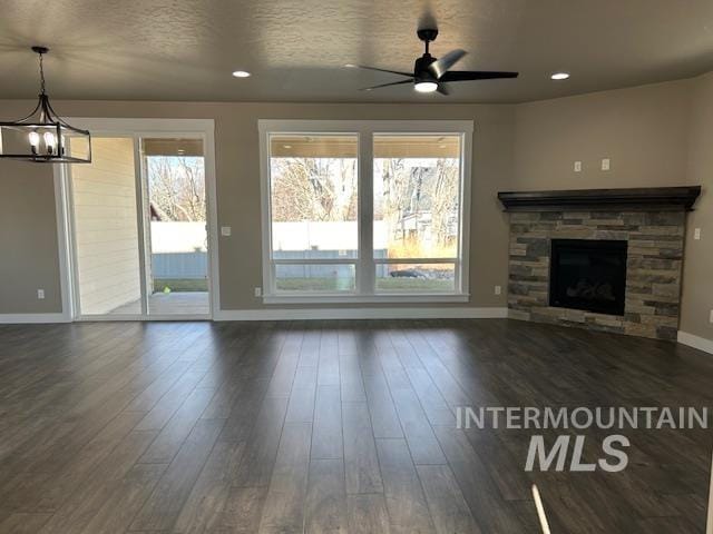 unfurnished living room with dark wood-type flooring, a wealth of natural light, and a stone fireplace