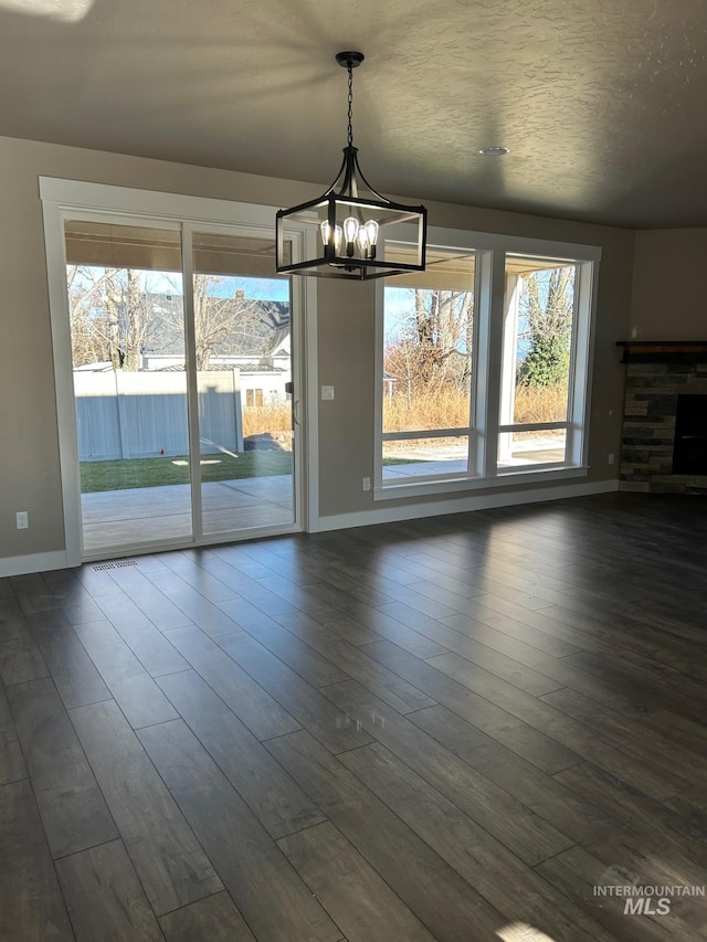 unfurnished dining area featuring dark wood-type flooring, an inviting chandelier, plenty of natural light, and a stone fireplace