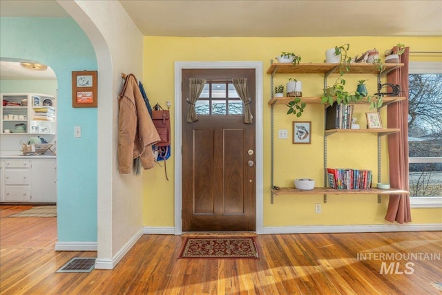 entrance foyer featuring arched walkways, wood finished floors, visible vents, and baseboards