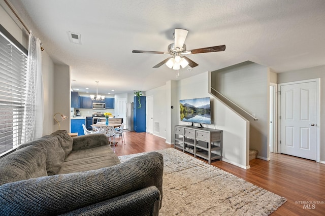 living room featuring ceiling fan with notable chandelier, dark hardwood / wood-style floors, and a textured ceiling