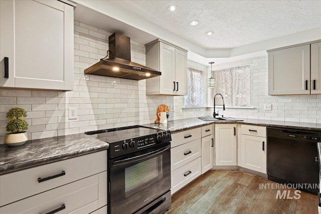 kitchen featuring dark stone countertops, black appliances, wall chimney range hood, and light wood-type flooring