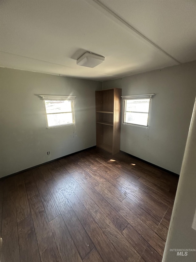 spare room with baseboards and dark wood-style flooring