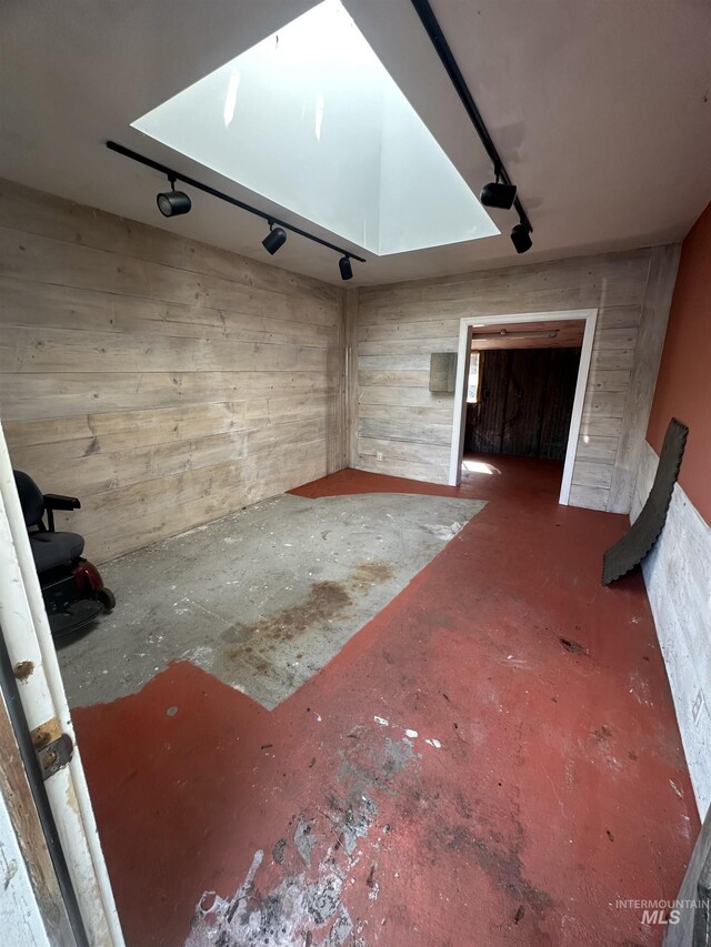 interior space featuring wooden walls, unfinished concrete flooring, and track lighting