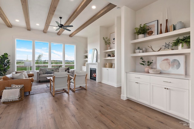 interior space with beamed ceiling, built in shelves, ceiling fan, and light hardwood / wood-style flooring